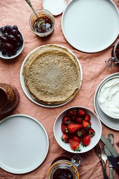 a table topped with plates and bowls filled with food next to utensils on top of a pink cloth