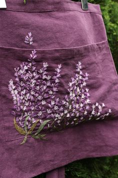 a purple skirt with lavender flowers embroidered on the front and side, hanging from a metal hook