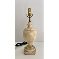 a white vase with a gold candle holder on it's base and a black cord attached to the top