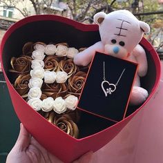 a teddy bear sitting inside of a heart shaped box filled with roses and a necklace