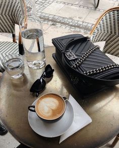 a cappuccino sits on a table next to a black purse and glasses