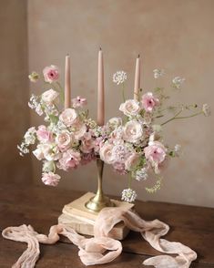 a vase filled with pink flowers and candles on top of a wooden table next to a scarf