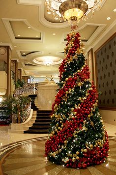 a decorated christmas tree in the middle of a lobby with stairs and chandelier