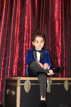 a young boy in a tuxedo sitting on top of a trunk