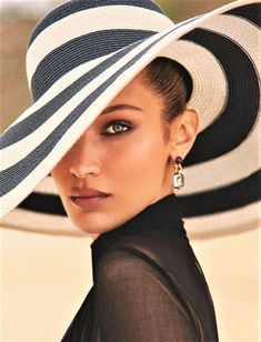 a woman wearing a white and black hat with stripes on the brim, looking at the camera