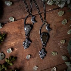 two necklaces on a wooden table with flowers and rocks in the background, one is holding an owl