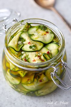 a jar filled with sliced cucumbers on top of a white counter next to a spoon