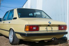 an old yellow bmw is parked in front of a white building with a blue sky behind it