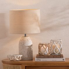 a table with a lamp and two candles on it next to a book, bowl and cup