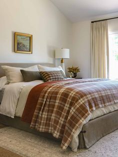 a bed with plaid comforter and pillows in a bedroom next to a large window