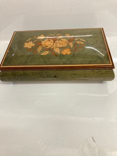 a green box with flowers painted on the side and gold trimming around the edges