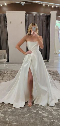 a woman taking a selfie while wearing a white wedding dress and high slit skirt