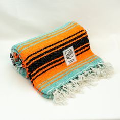 an orange and black striped towel with fringes on the bottom, sitting on a white surface