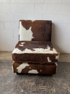 a brown and white cowhide chair against a brick wall