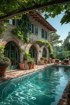 an outdoor swimming pool surrounded by potted plants and greenery next to a stone house