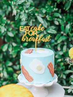 a blue cake with bacon on it and a sign that says eat for breakfast next to some flowers