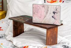 a laptop computer sitting on top of a wooden table in front of a white bed