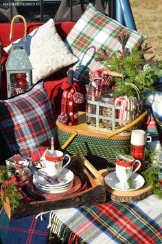 a picnic table with plaid blankets, cups and saucers on it is set up for christmas