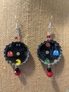 a pair of black bottle caps with pacman charms hanging from them