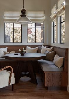 a corner table and bench in a living room with two windows above the couches