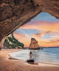 a person standing on the beach in front of an arch