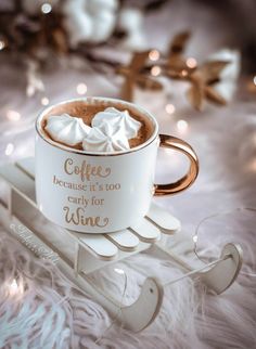 a coffee mug with whipped cream in it on a white fur covered tablecloth next to christmas lights