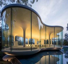 a curved building with glass walls next to a body of water