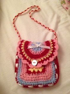 a crocheted purse sitting on top of a white bed next to a pillow