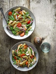 two bowls filled with pasta salad on top of a wooden table