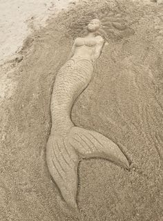 a sand sculpture of a mermaid laying on the beach with her head in the sand