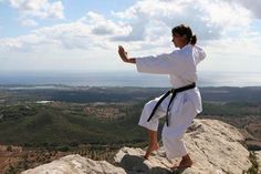 a woman doing karate on top of a rocky cliff overlooking a valley and mountains in the distance