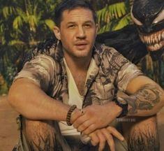 a man with tattoos on his arms sitting in front of some trees and palm trees