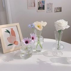 three glass vases with flowers in them on a table next to a framed photograph