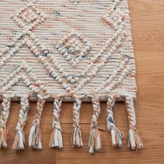 a white rug with tassels on top of a wooden floor next to a wood floor