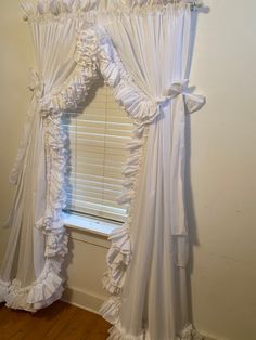 a white curtain with ruffles hanging from it's side in front of a window