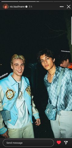 two young men standing next to each other in front of a dark background, one is wearing a blue shirt and the other has white pants