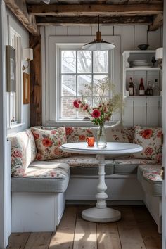 a white table sitting under a window next to a wooden bench with flowers on it