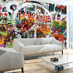 a living room filled with white furniture and graffiti covered wall behind the couch is a glass coffee table