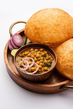 two bread rolls and a bowl of chickpeas on a wooden plate