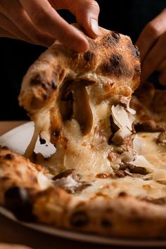 a person is taking a slice of mushroom pizza from a white plate on a wooden table