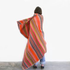 a woman standing against a wall wearing an orange and pink striped ponchy shawl