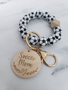 the soccer mom charm bracelet is shown on a marble surface with a gold plated keychain