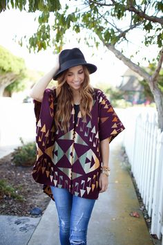 a woman is walking down the sidewalk wearing a hat and a ponchy top