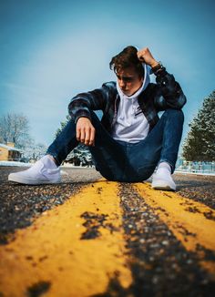 a young man sitting on the side of an empty road