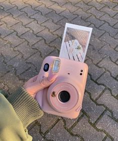 a person holding up a pink camera with an instax card attached to it