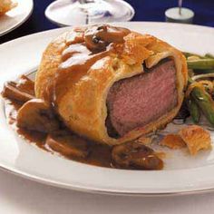 a white plate topped with meat and gravy covered in sauce next to asparagus