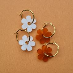 two pairs of flower shaped hoop earrings sitting on top of an orange surface next to each other