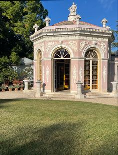 a pink building with statues on the top and windows in it's center surrounded by grass