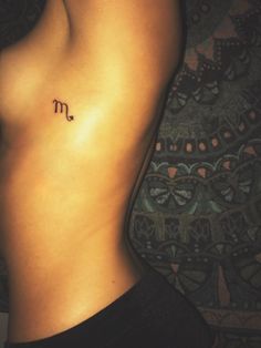 a woman's stomach with the letter m tattooed on her left side ribcage