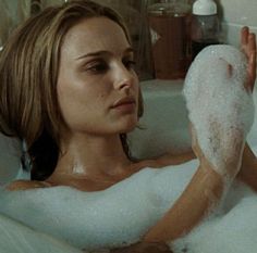 a woman sitting in a bathtub with foam on her feet and holding something up to her face